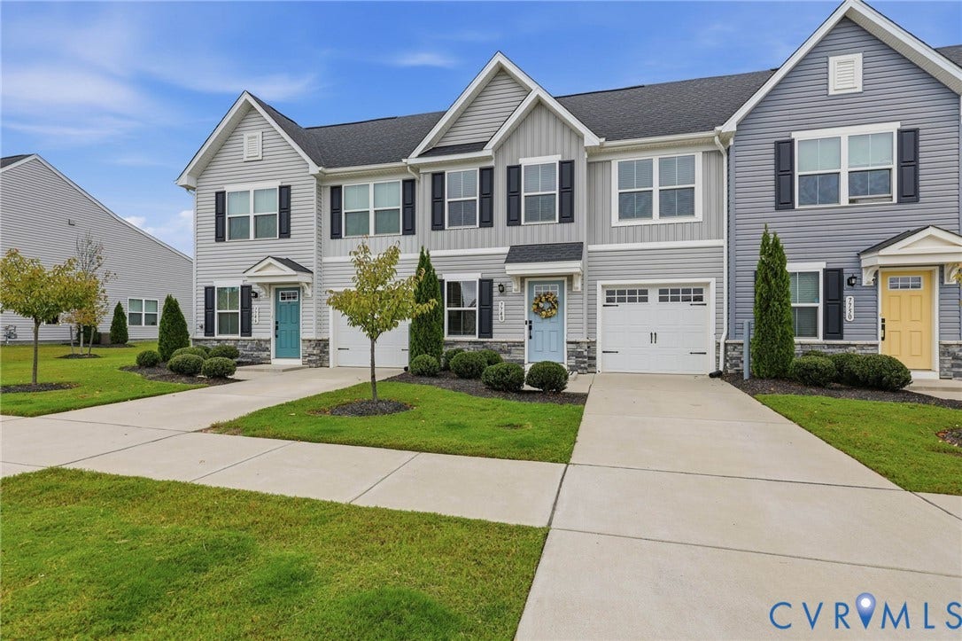 Multi-unit exterior featuring gray horizontal siding, stone veneer accents, individual concrete driveways, single-car garages, and decorative window shutters