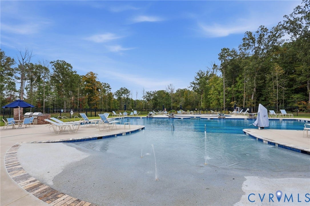Outdoor swimming pool featuring a zero-entry design with integrated water jets, stone-finish masonry, concrete decking, and a brick-encased built-in grilling station