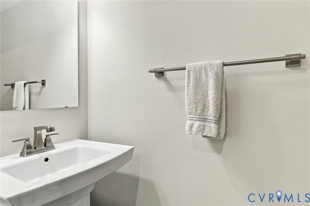 Wall-mounted pedestal sink featuring a centered basin and a metallic dual-handle faucet, complemented by a flat-panel frameless mirror and a brushed-nickel towel bar