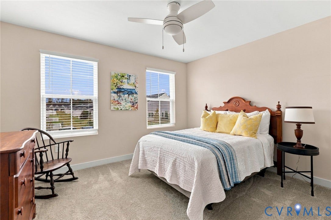 Neutral-toned bedroom featuring carpeted flooring, dual windows with horizontal blinds, and a white ceiling fan with integrated lighting