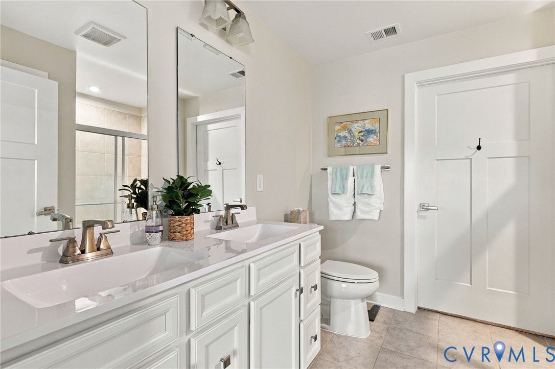 Double vanity featuring white cabinetry, integrated sinks, solid surface countertops, polished metal fixtures, and dual framed mirrors