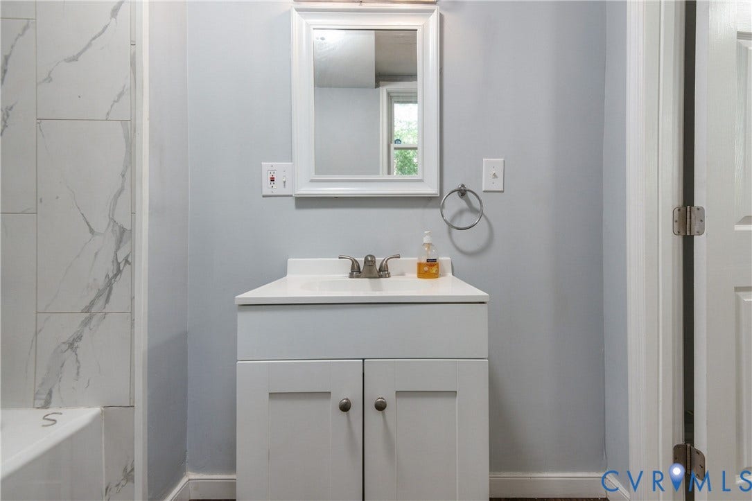 113 Spring Street, Pembroke, Petersburg, VA 23803 White vanity cabinet with an integrated rectangular basin, chrome dual-handle faucet, framed wall mirror, and floor-to-ceiling tile shower surround