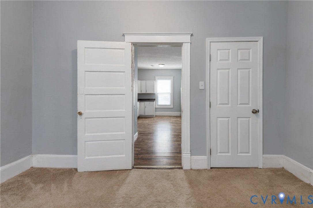 113 Spring Street, Pembroke, Petersburg, VA 23803 Interior space featuring neutral wall paint, white-painted wood trim, a four-panel door, a six-panel door, and wood-finish flooring visible through the doorway
