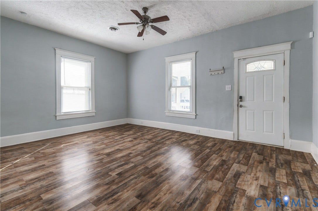 113 Spring Street, Pembroke, Petersburg, VA 23803 Room featuring wood-finish flooring, two windows with white trim, a multi-pane entry door with glass transom, and a central ceiling fan with integrated lighting