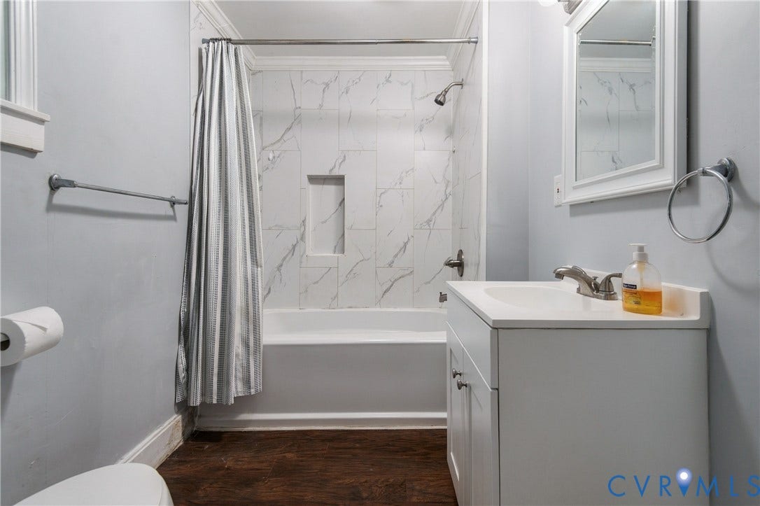 113 Spring Street, Pembroke, Petersburg, VA 23803 Bathroom featuring wood-finish flooring, a white vanity with an integrated countertop, tub-shower combination with full-height stone-patterned wall tile, and a built-in recessed shower niche