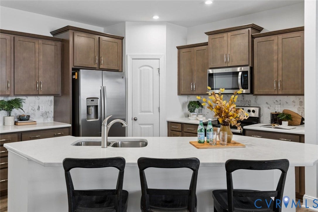 6177 Bowline Lane, Chesterfield, VA 23234 Kitchen featuring wood-finish cabinetry, stainless steel appliances, quartz island with an integrated sink, and a patterned backsplash.