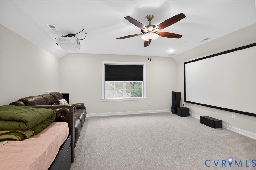 Multi-purpose room featuring a wall-mounted projector screen, integrated ceiling-mounted projector, wall-to-wall carpeting, and a central ceiling fan with integrated lighting