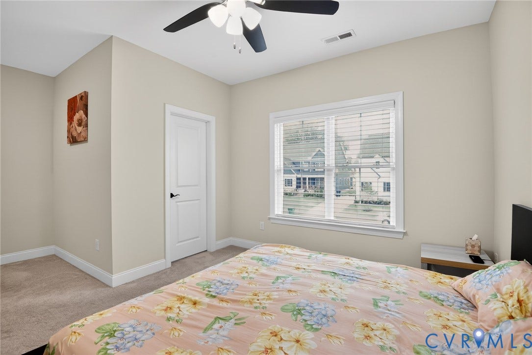 Neutral wall tones, carpeted flooring, multi-pane window with blinds, and a ceiling fan with integrated lighting