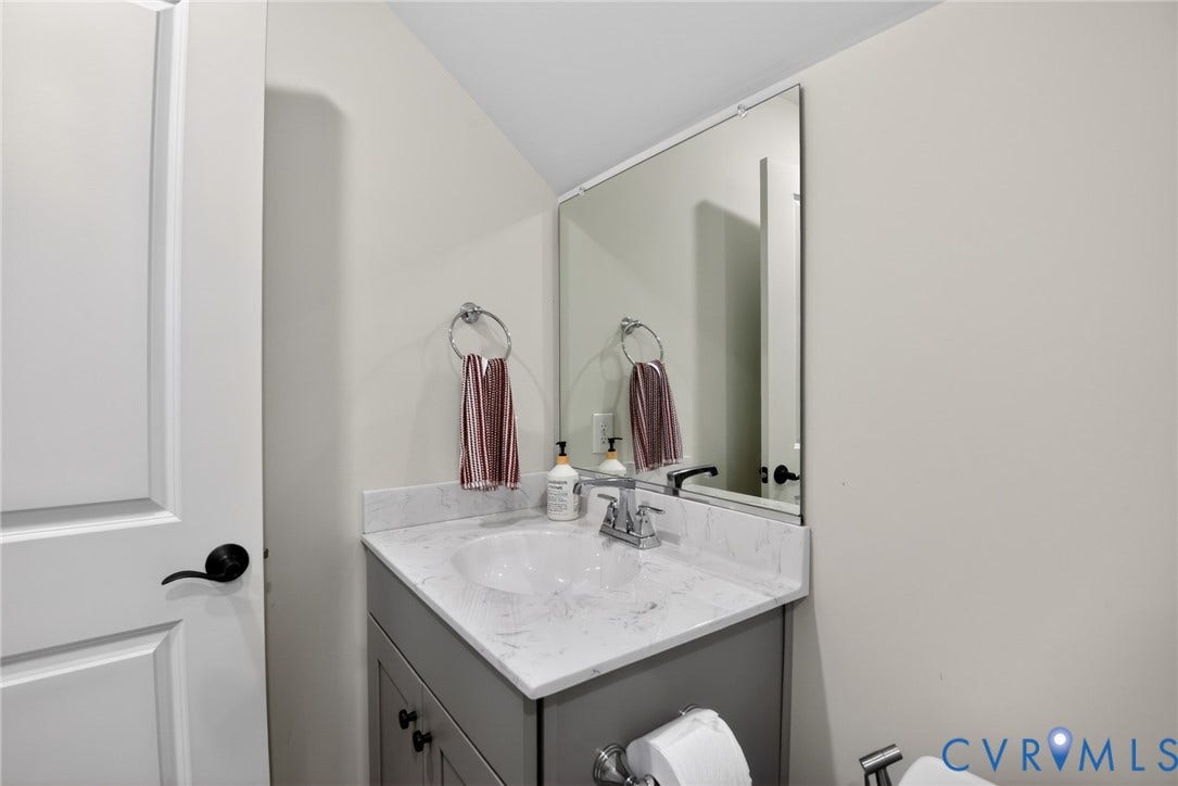 Grey vanity featuring a stone-composite countertop with integrated sink, chrome-finish faucet, rectangular frameless mirror, and circular towel ring