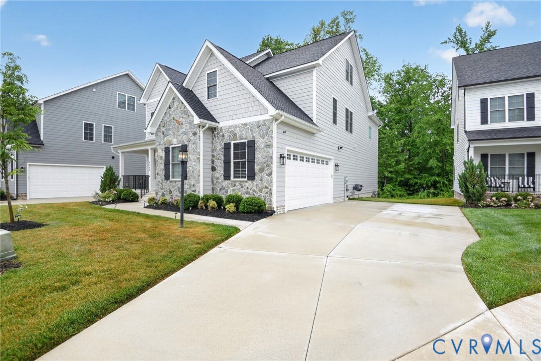 Multi-story residence featuring light gray siding with stone veneer facade, asphalt shingle roofing, attached two-car garage, and concrete driveway
