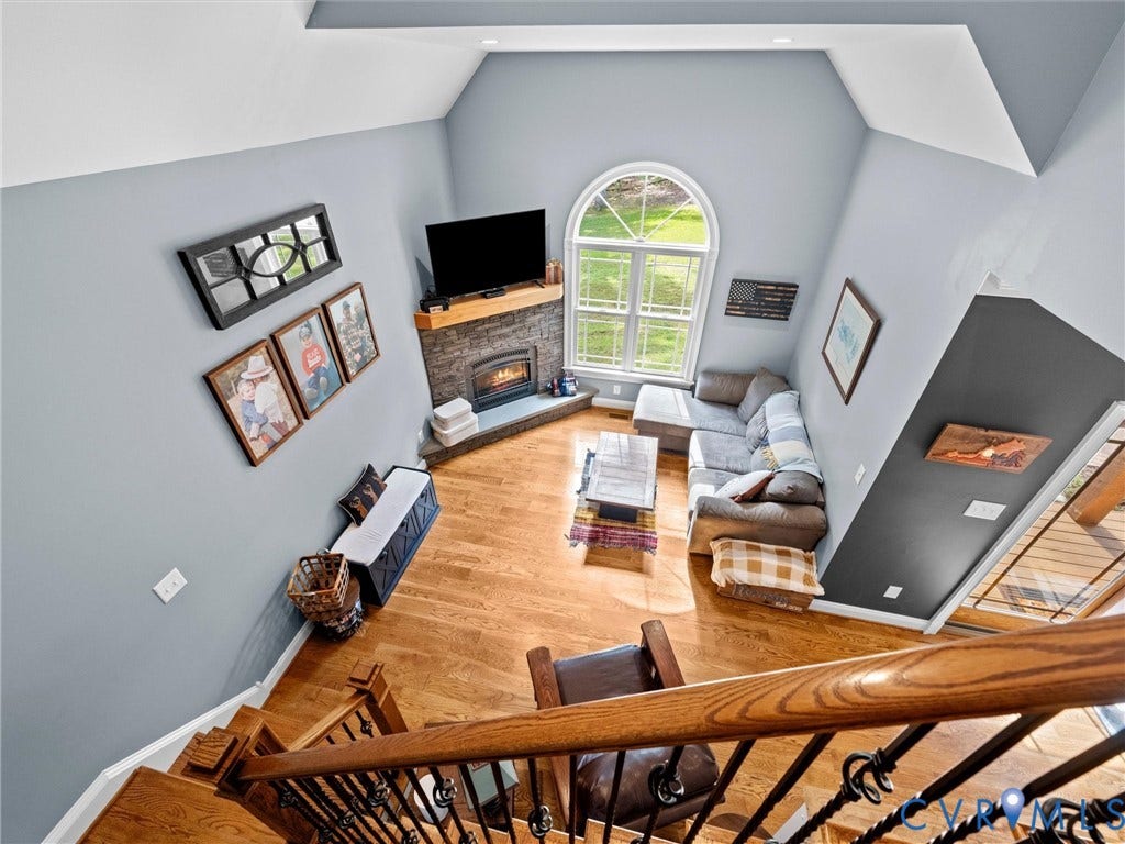 9877 Swinging Bridge Road, Taylors Grove Estates, Quinton, VA 23141 A beautiful view from the upper level overlooks the spacious two-story family room, showcasing the soaring ceilings, dramatic arched window, stacked stone gas fireplace, and gleaming hardwood floors. An open, airy design filled with natural light!