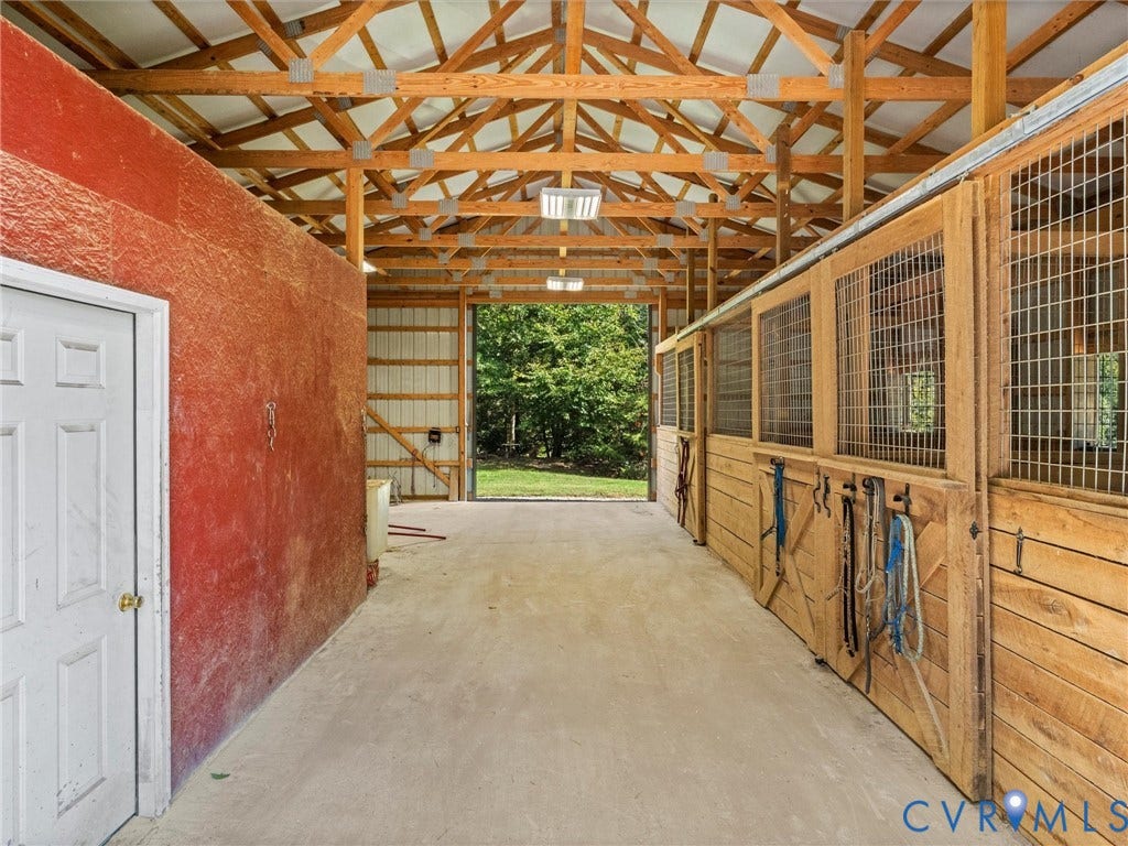 9877 Swinging Bridge Road, Taylors Grove Estates, Quinton, VA 23141 Another view of the spacious barn aisle showcases the exposed wood trusses, attractive stall fronts, and convenient tack room access. The open layout provides plenty of room for grooming, tacking up, and everyday horse care!