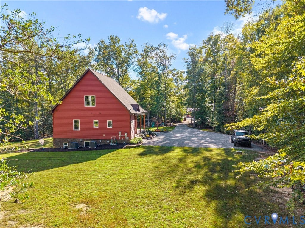 9877 Swinging Bridge Road, Taylors Grove Estates, Quinton, VA 23141 A picturesque side view of the home showcases the expansive green lawn, mature shade trees, and beautifully maintained landscaping. The spacious gravel parking area and peaceful wooded surroundings add to the charm and convenience of this country retreat!