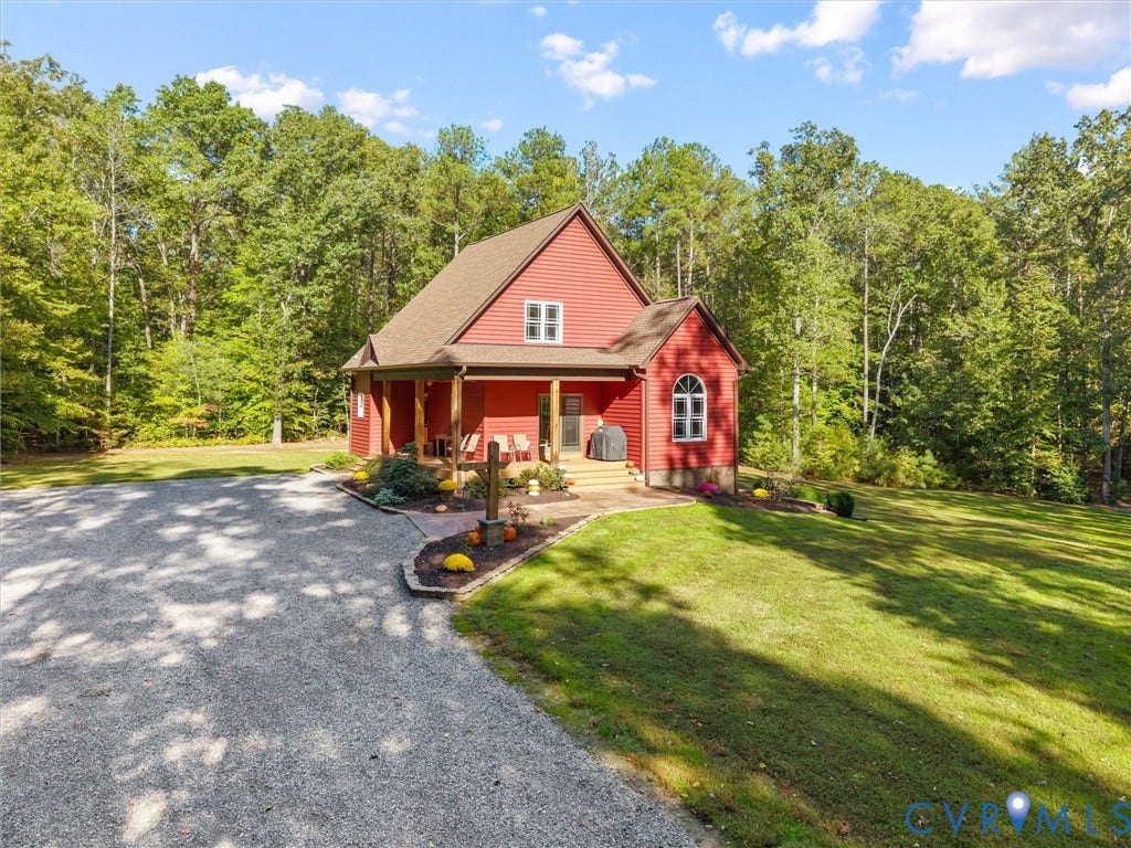 9877 Swinging Bridge Road, Taylors Grove Estates, Quinton, VA 23141 A welcoming approach to The Little Red Homestead showcases the charming covered front porch with beautiful white oak posts, attractive landscaping, and ample gravel parking. Surrounded by mature trees, this picturesque setting offers both convenience and country charm!