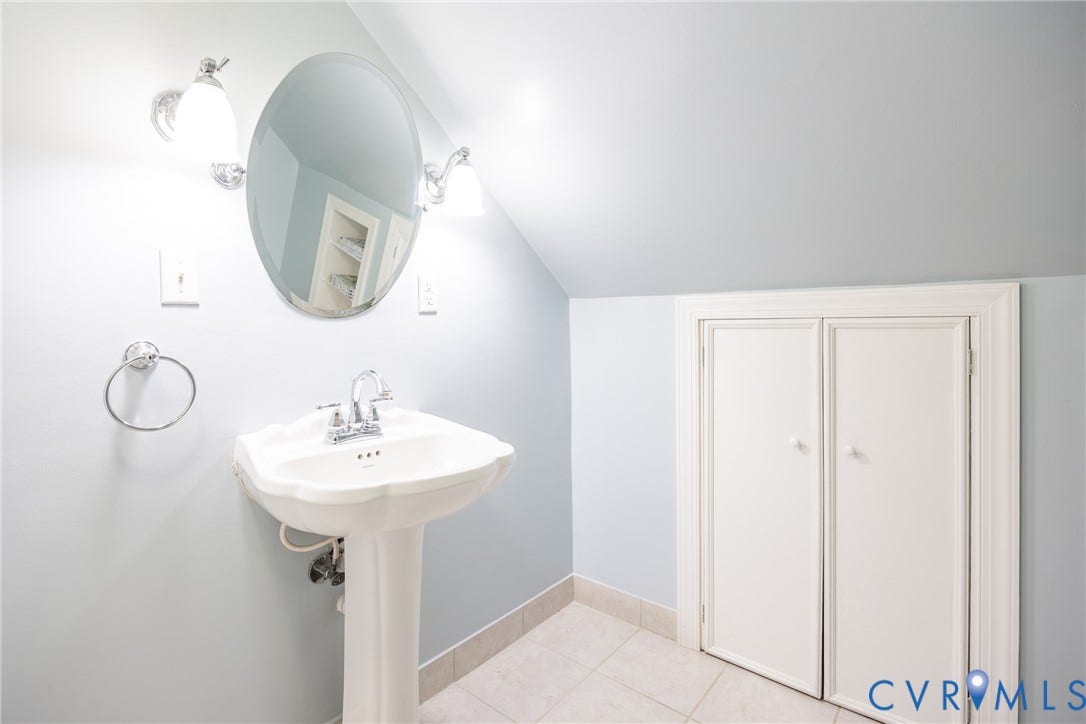 6614 Monument Avenue, Westhaven, Henrico, VA 23226 White pedestal sink with chrome faucet, oval wall-mounted mirror, dual globe wall sconces, and built-in under-eave storage cabinetry