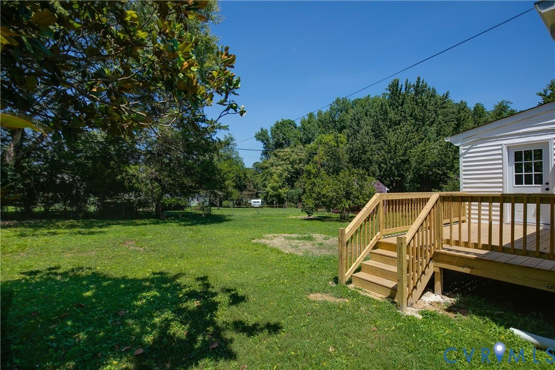 7263 Grace Lane, Mechanicsville, VA 23111 Expansive backyard featuring a new wood deck with stairs, white siding exterior, and mature trees surrounding the perimeter