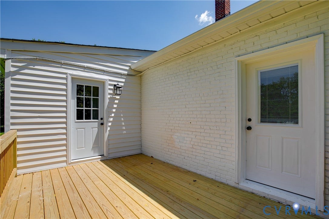 7263 Grace Lane, Mechanicsville, VA 23111 Expansive wooden deck with natural finish, featuring two white entry doors with glass lites, a white brick exterior, and white vinyl siding