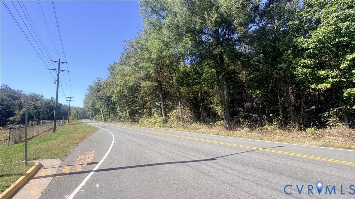 Paved asphalt road frontage bordered by dense mature trees and cleared grass terrain