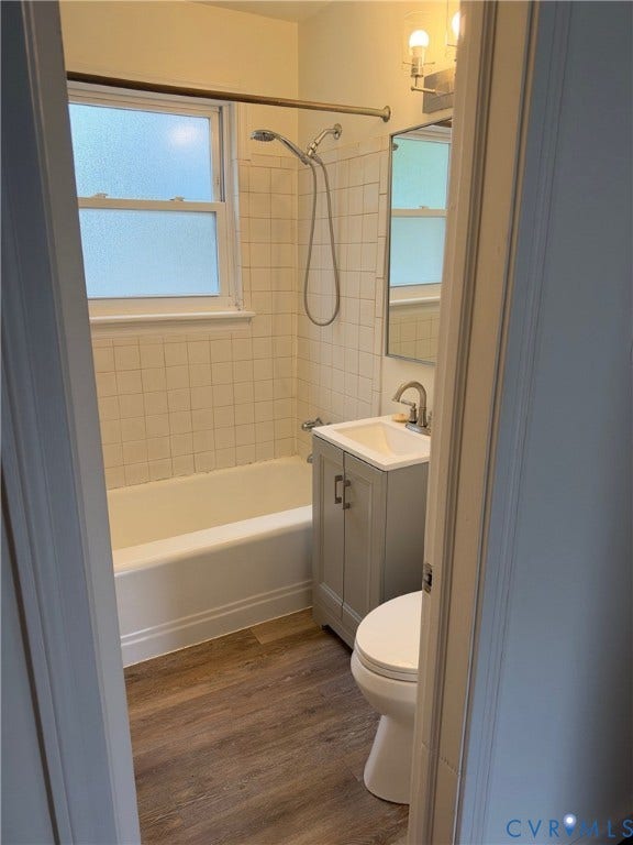 6523 Stuart Avenue, Richmond, VA 23226 Bathroom featuring a wood-finish floor, white porcelain tub with square tile surround, single-basin vanity, and a rectangular wall-mounted mirror