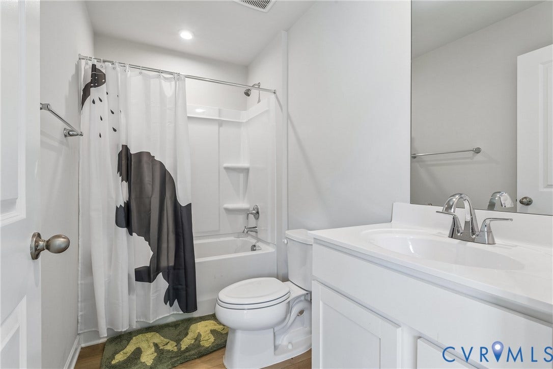 Full bathroom featuring a white vanity with a composite countertop and integrated sink, chrome faucet, wall-spanning mirror, and a tub-shower combination with white surround