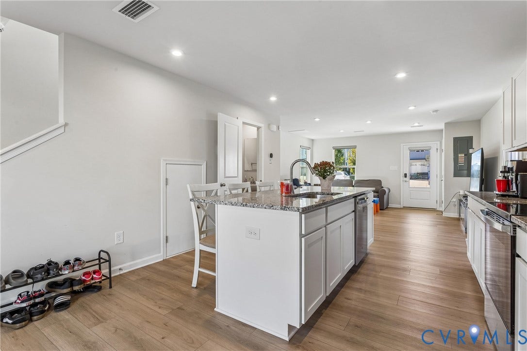 Kitchen featuring a stone-topped island with an integrated stainless-steel sink, shaker-style white cabinetry, wood-finish flooring, recessed lighting, and stainless-steel appliances