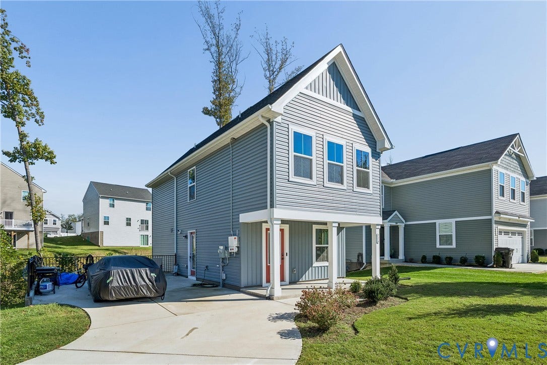 Two-story residence featuring grey horizontal lap siding, a front porch with square columns, a steep gabled roofline, and a concrete driveway