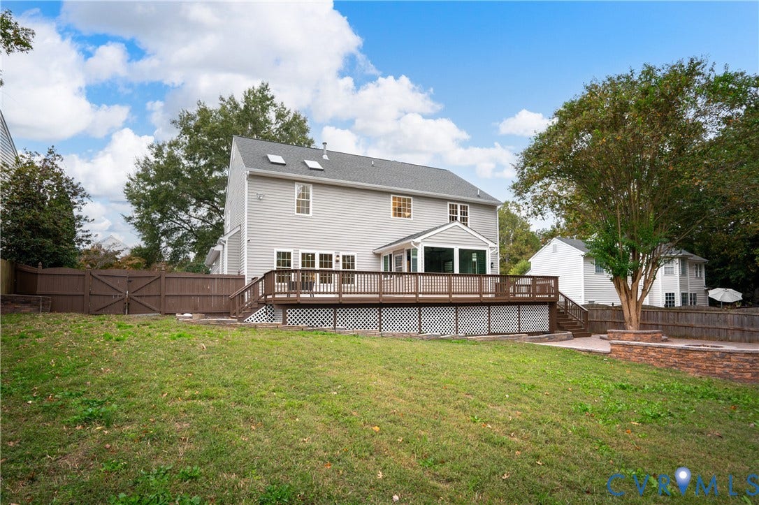 8060 Pebblepath Parkway, Hanover, VA 23111 Rear exterior featuring a grey-sided two-story home, elevated wooden deck with lattice skirting, skylights, enclosed sunroom, and privacy wood fencing
