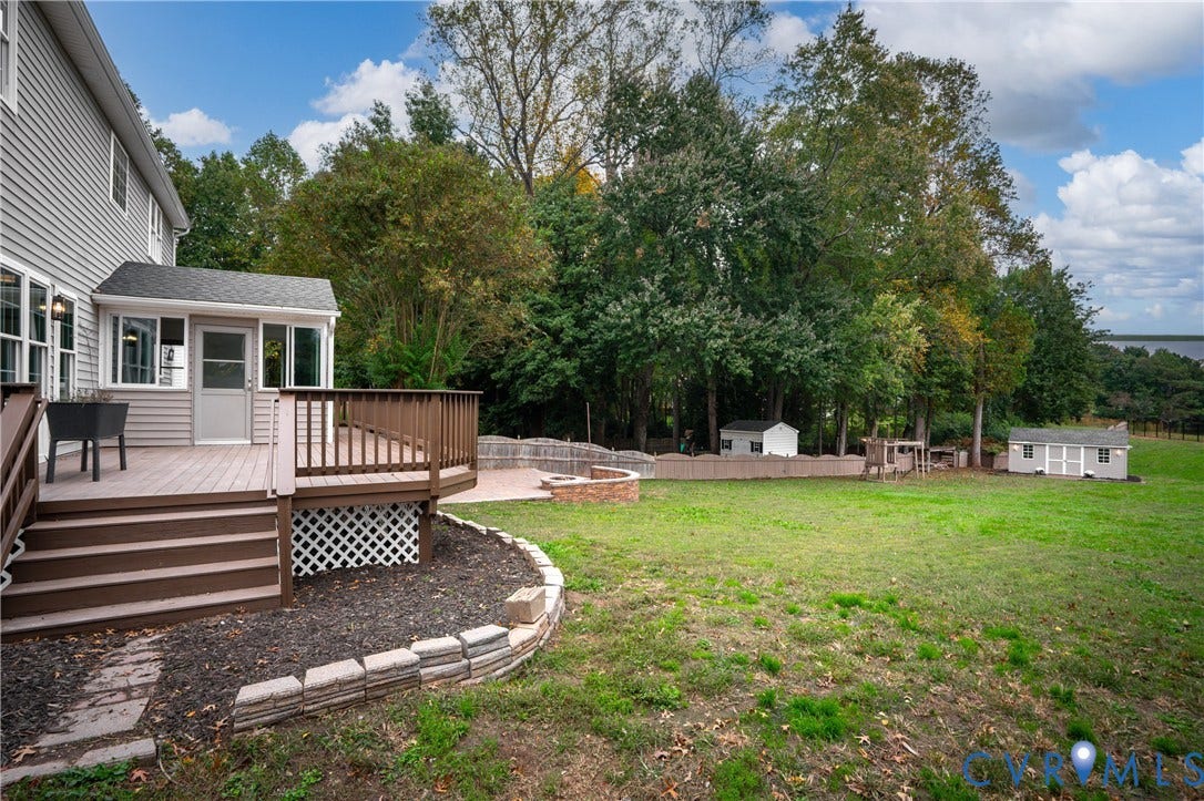8060 Pebblepath Parkway, Hanover, VA 23111 Raised deck featuring horizontal railings and lattice skirting, stone fire pit, paved patio area, and mature perimeter trees