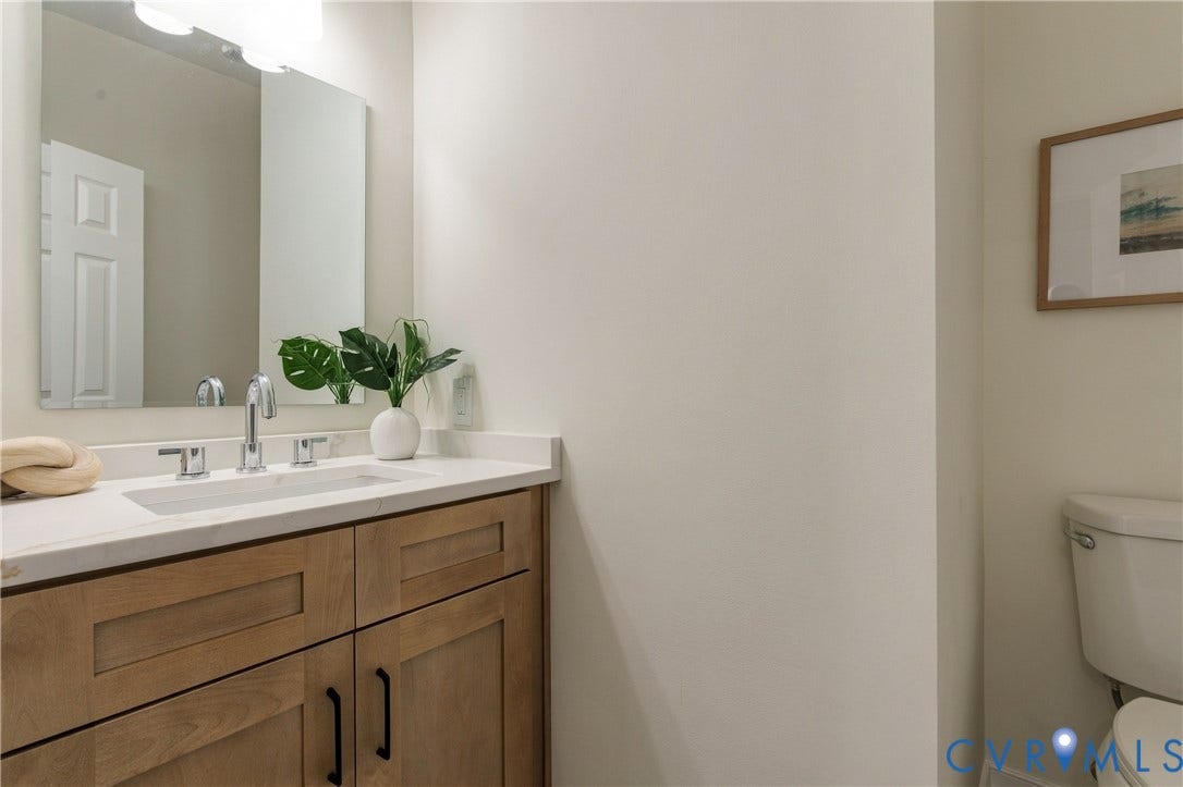 8060 Pebblepath Parkway, Hanover, VA 23111 Bathroom featuring a wood-finish vanity with shaker-style cabinetry, white countertop with an integrated rectangular sink, chrome widespread faucet, large frameless wall mirror, and high-mounted vanity lighting