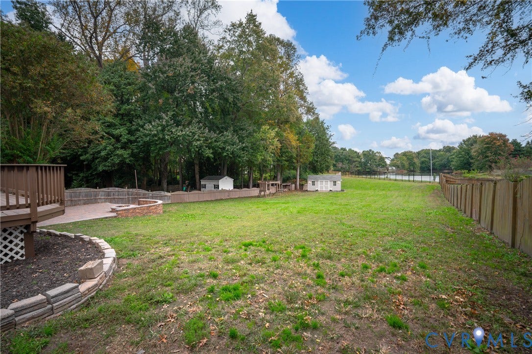 8060 Pebblepath Parkway, Hanover, VA 23111 Expansive backyard featuring a tiered wooden deck, stone-bordered landscape beds, a brick retaining wall, and peripheral wood fencing
