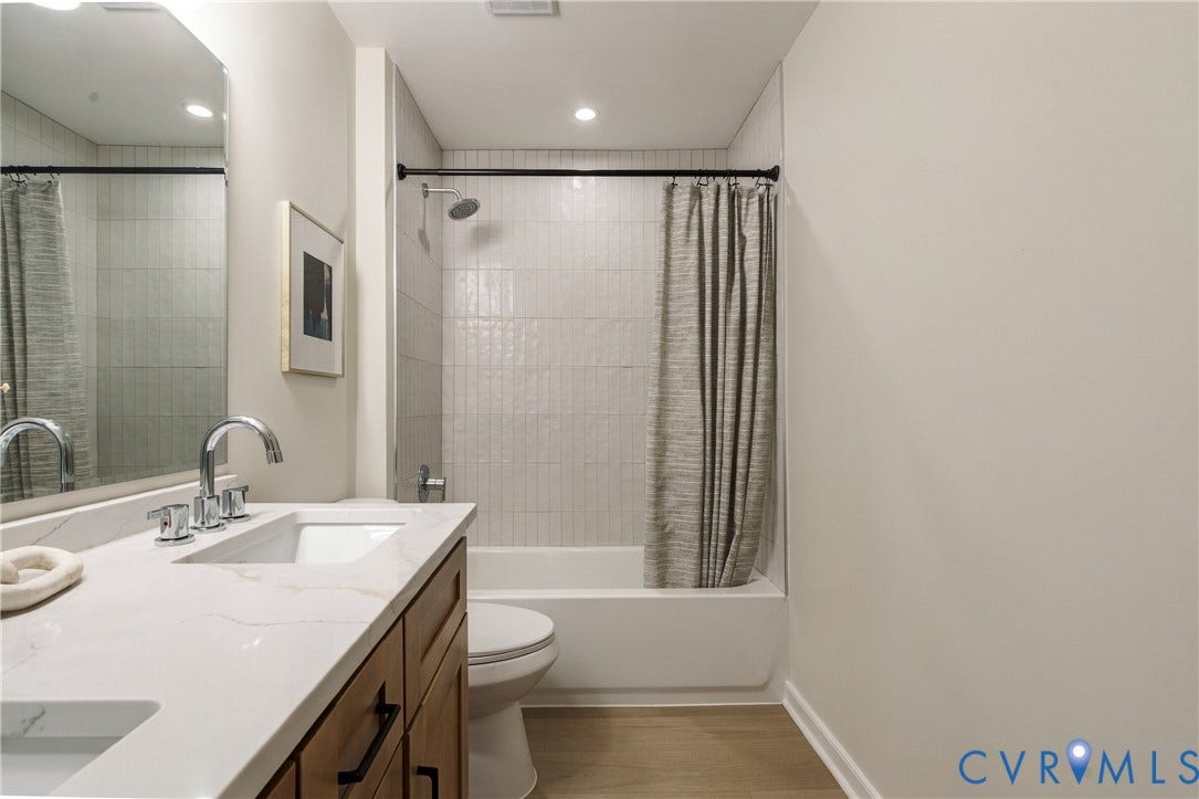 8060 Pebblepath Parkway, Hanover, VA 23111 Bathroom featuring a vanity with white stone-finish countertop, dual under-mount sinks, chrome widespread faucets, wood-finish cabinetry, and a tub-shower combination with floor-to-ceiling tile surround