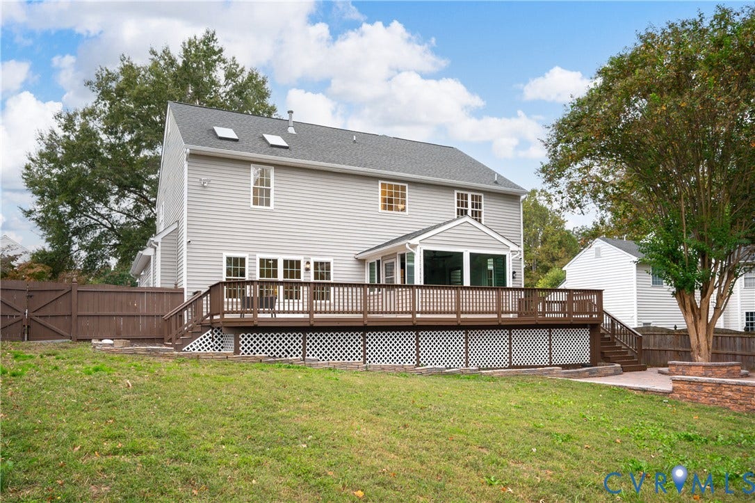 8060 Pebblepath Parkway, Hanover, VA 23111 Rear exterior featuring gray siding, a raised wood deck with lattice skirting, an enclosed sunroom, two roof skylights, and perimeter wood fencing