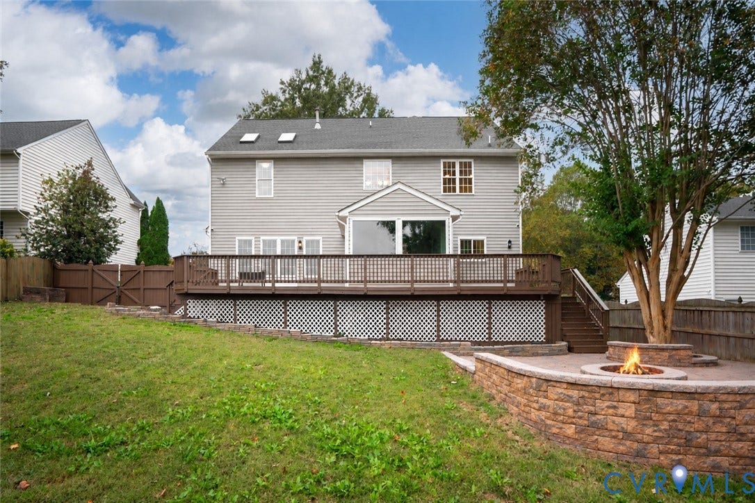 8060 Pebblepath Parkway, Hanover, VA 23111 Rear exterior featuring a tiered wooden deck with lattice skirting, paver patio, stone-finish circular fire pit, and privacy fencing