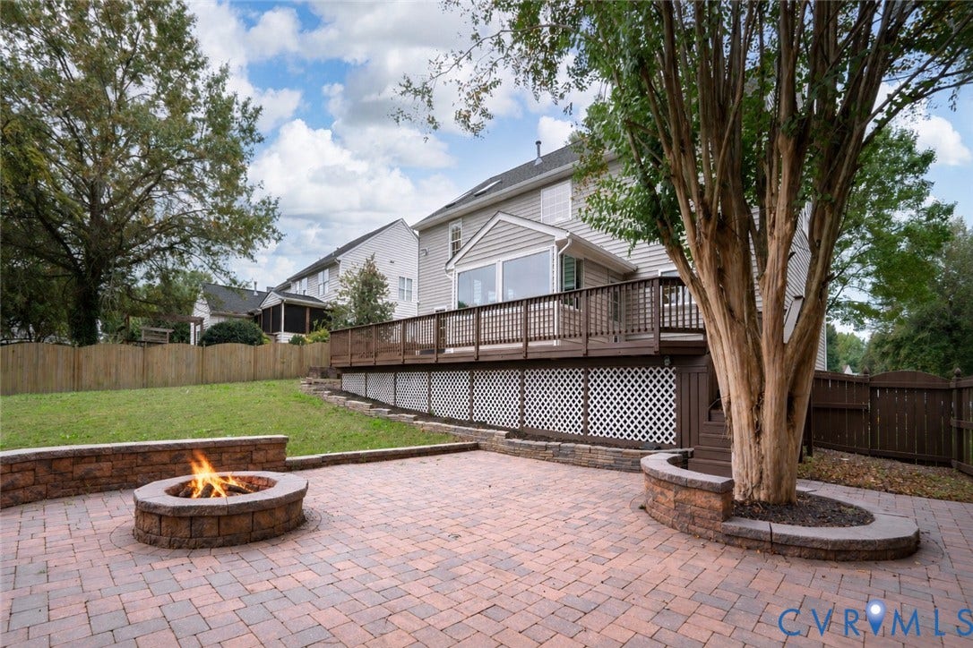 8060 Pebblepath Parkway, Hanover, VA 23111 Backyard featuring a paved stone patio, built-in stone fire pit, tiered raised stone planter, elevated wood deck with lattice skirting, and wood privacy fencing