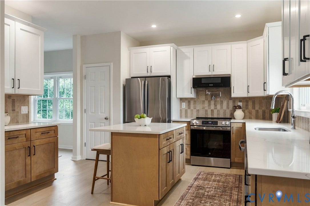 8060 Pebblepath Parkway, Hanover, VA 23111 Kitchen featuring white shaker-style upper cabinetry, contrasting wood-finish base cabinets, a central island with a solid surface countertop, stainless steel appliances, and tile backsplash