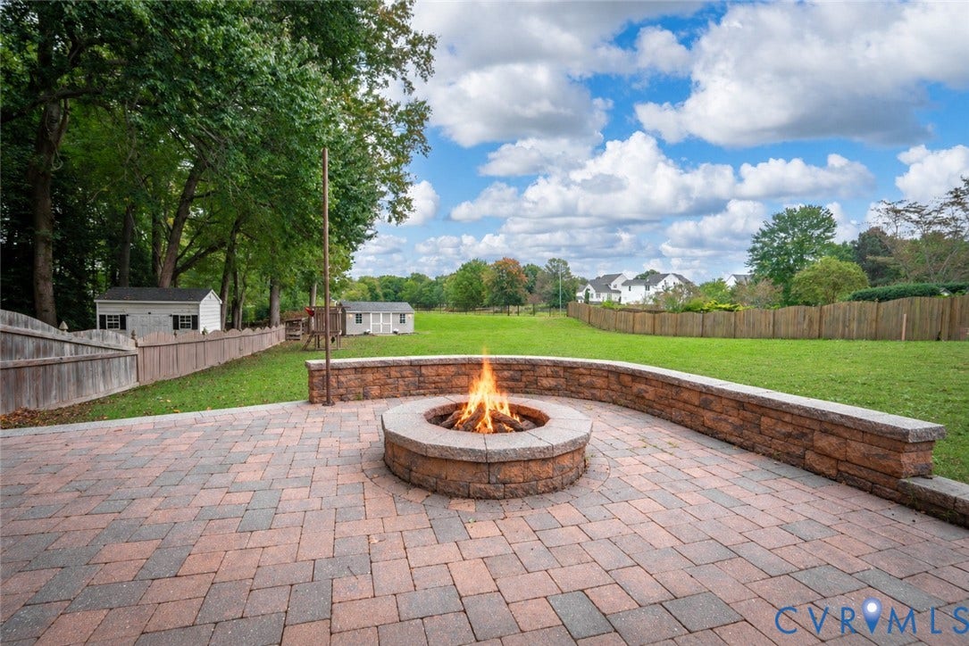 8060 Pebblepath Parkway, Hanover, VA 23111 Paver patio featuring a circular stone fire pit and a curved retaining wall bordering a fenced-in grassy lawn
