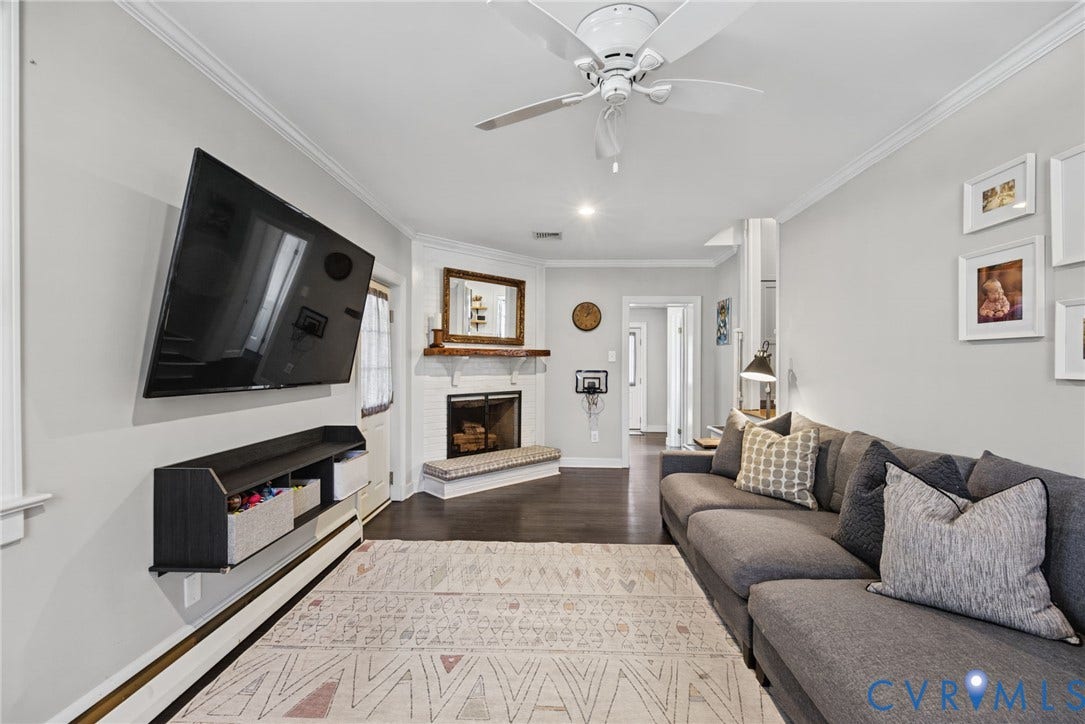 1009 Malvern Avenue, Malvern Gardens, Richmond, VA 23221 Corner fireplace featuring a painted brick hearth and wood mantel, white crown molding, wood-finish flooring, and a ceiling fan with integrated lighting