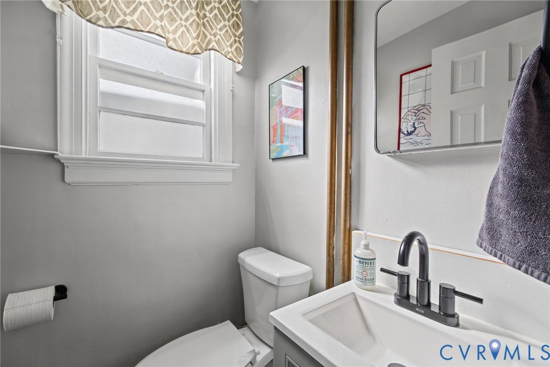 1009 Malvern Avenue, Malvern Gardens, Richmond, VA 23221 Bathroom featuring a vanity with a white integrated basin, matte black widespread faucet, rectangular wall-mounted mirror, and a double-hung window with decorative trim