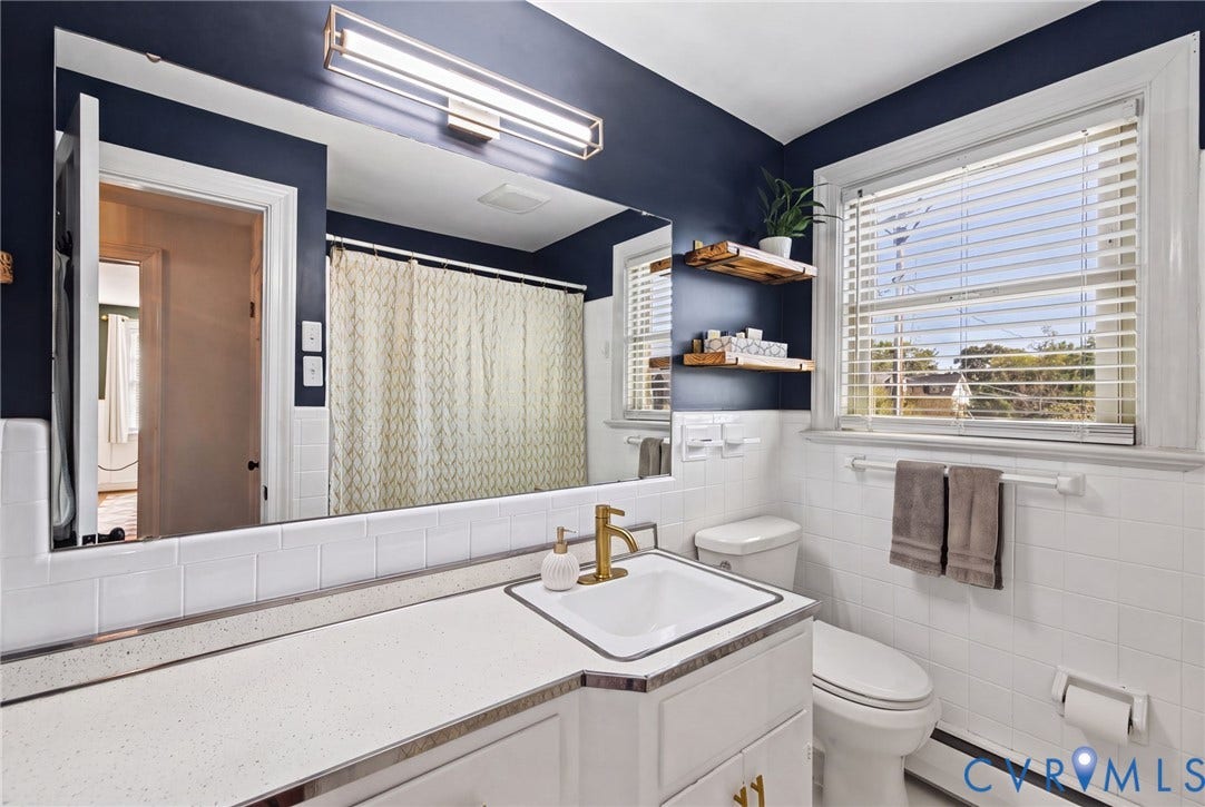 1009 Malvern Avenue, Malvern Gardens, Richmond, VA 23221 Bathroom featuring a white vanity with a solid-surface countertop, rectangular undermount sink with a brass-finish faucet, oversized wall-to-wall vanity mirror, and white tile wainscoting