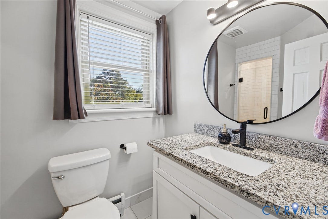 1009 Malvern Avenue, Malvern Gardens, Richmond, VA 23221 Bathroom vanity featuring a speckled stone countertop, white shaker-style cabinetry, a round mirror, and a matte black single-handle faucet