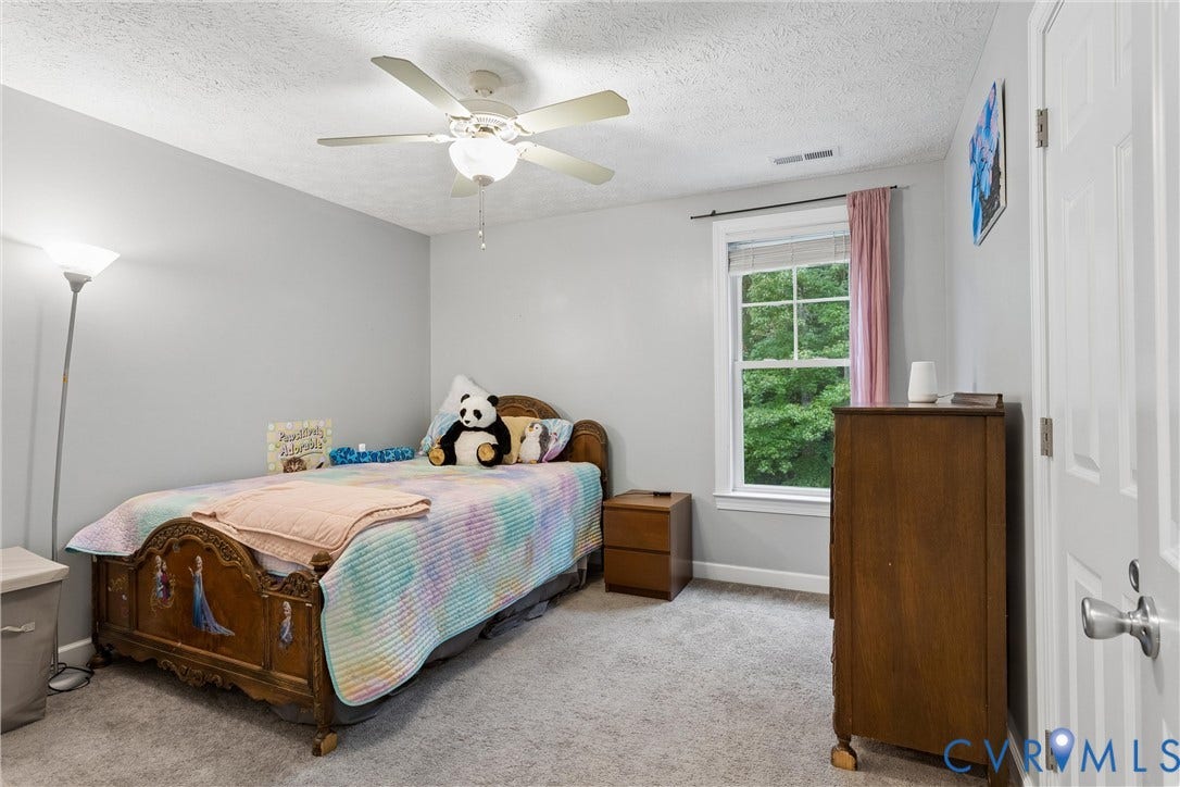 Neutral-toned interior featuring wall-to-wall carpeting, a multi-pane window with exterior greenery, and a ceiling-mounted fan with integrated lighting
