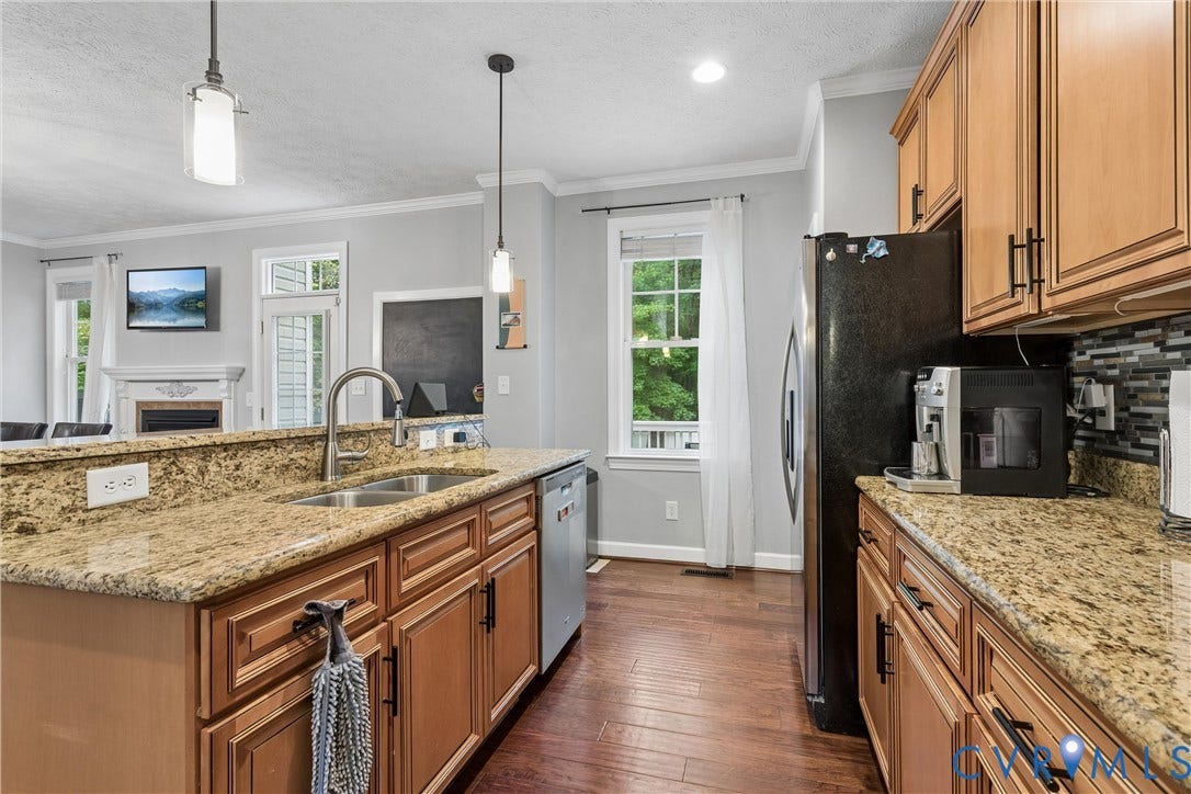 Kitchen featuring stained wood cabinetry, stone countertops, wood-finish flooring, stainless steel under-mount sink with high-arc faucet, and pendant lighting