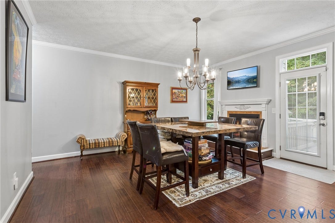 Dining area featuring dark wood-finish flooring, a traditional fireplace with a decorative mantel, a multi-arm chandelier, and a glass-paneled exterior door