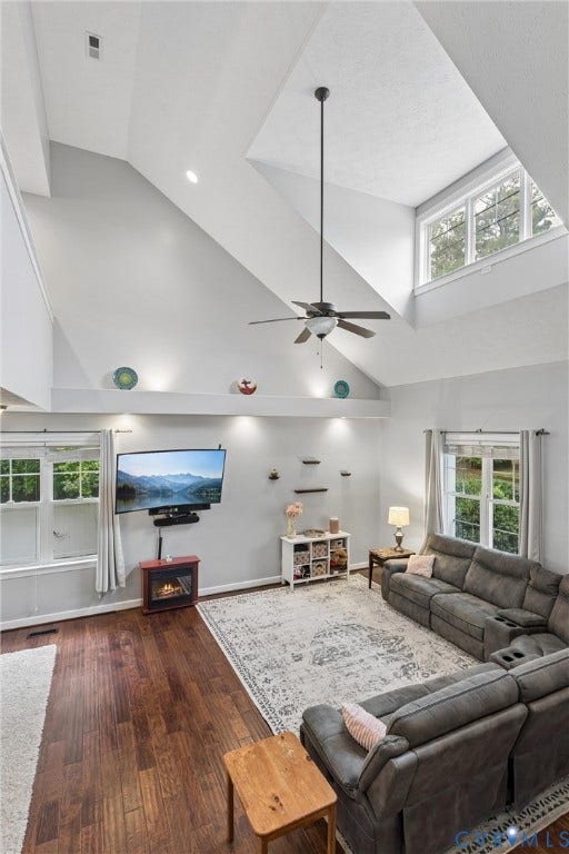 Vaulted ceilings featuring expansive windows, recessed architectural shelving, dark wood-finish flooring, and a ceiling fan