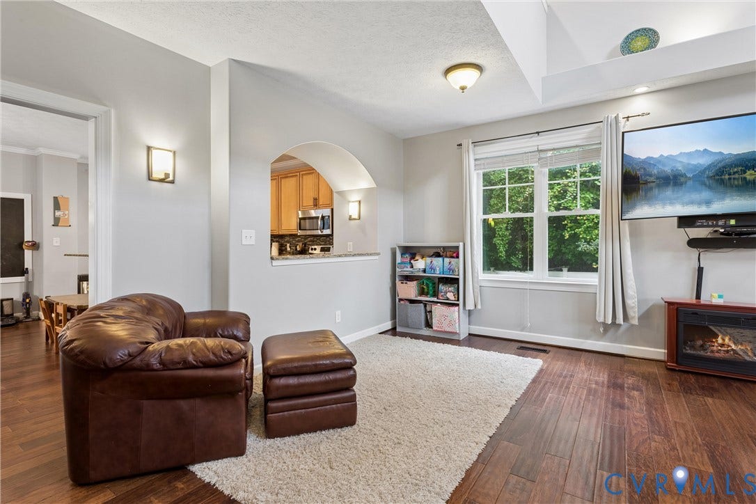 Living area featuring vaulted ceilings, wood-finish flooring, an arched wall cutout, and a mounted electric fireplace