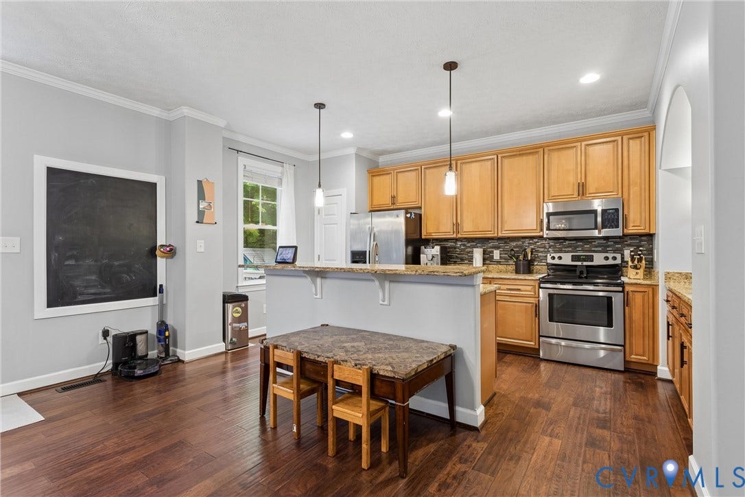 Kitchen featuring wood cabinetry, stainless steel appliances, stone-finish countertops, tile backsplash, and wood-finish flooring