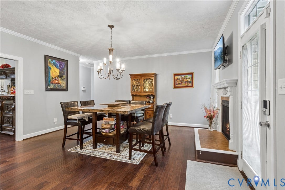 Wood-finish flooring, fireplace with a decorative mantel, and multi-arm chandelier lighting