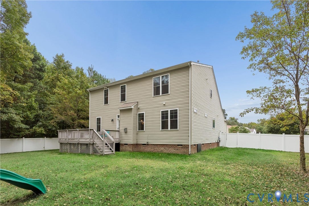 Two-story residence featuring light-toned vinyl siding, a brick foundation, a wood-deck platform with stairs, and a full-perimeter white vinyl fence