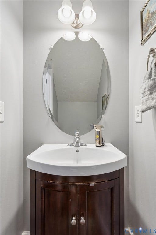 Oval wall-mounted mirror featuring polished edges, two-light fixture with glass shades, wood-finish vanity cabinet, and white basin with a single-handle faucet