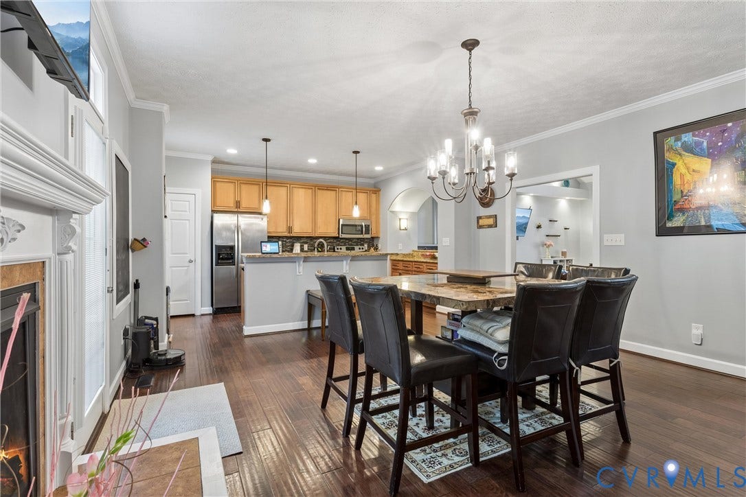 Open-concept floor plan featuring dark wood-finish flooring, a kitchen with wood cabinetry and stainless steel appliances, crown molding, a decorative fireplace, and a traditional-style chandelier